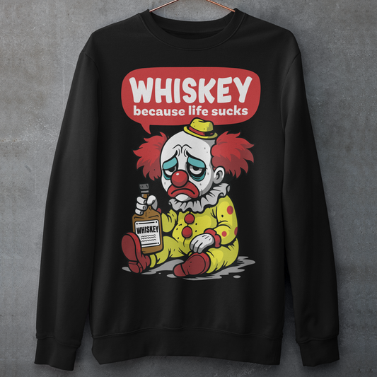 Black sweatshirt featuring a sad cartoon clown with messy red hair and a tired expression, sitting on the ground holding a bottle labeled whiskey. Above the character, bold text reads “Whiskey because life sucks.” The design combines dark humor with a playful cartoon style, creating a sarcastic and slightly edgy visual.