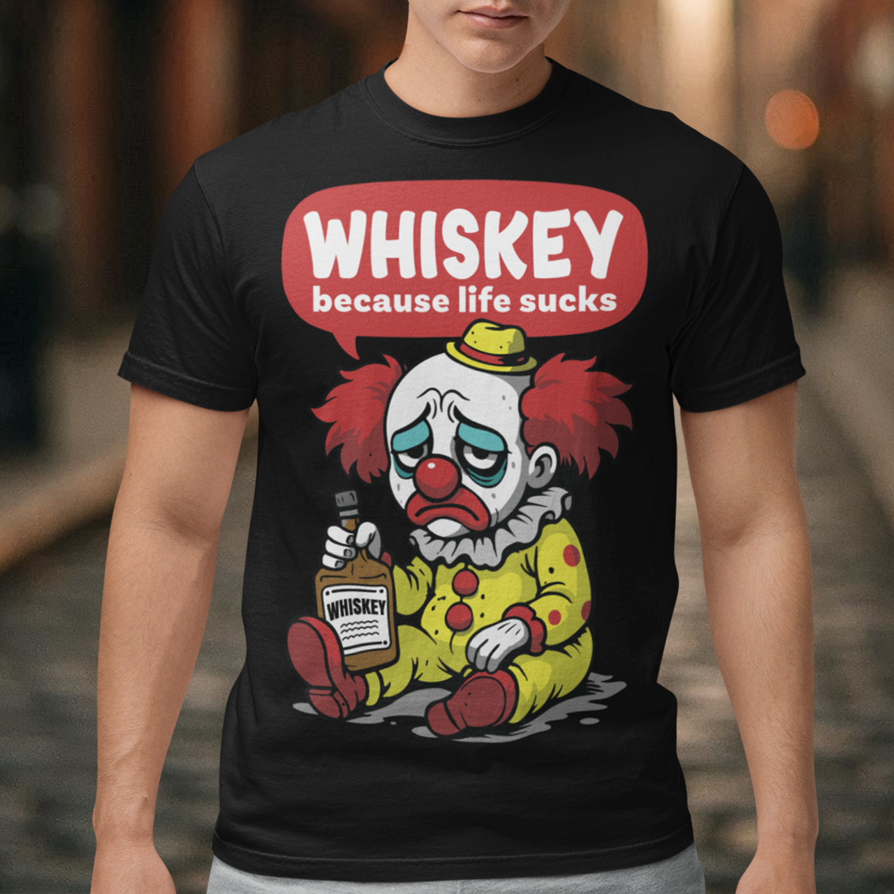 Black t-shirt featuring a sad cartoon clown with messy red hair and a tired expression, sitting on the ground holding a bottle labeled whiskey. Above the character, bold text reads “Whiskey because life sucks.” The design combines dark humor with a playful cartoon style, creating a sarcastic and slightly edgy visual.