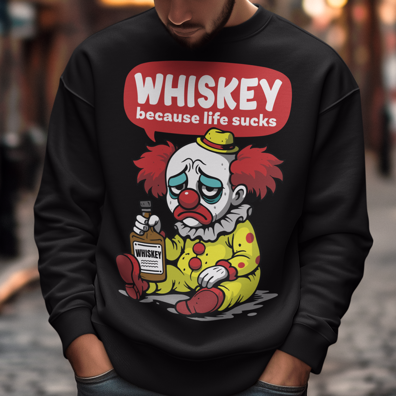 Black sweatshirt featuring a sad cartoon clown with messy red hair and a tired expression, sitting on the ground holding a bottle labeled whiskey. Above the character, bold text reads “Whiskey because life sucks.” The design combines dark humor with a playful cartoon style, creating a sarcastic and slightly edgy visual.