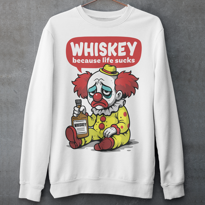 White sweatshirt featuring a sad cartoon clown with messy red hair and a tired expression, sitting on the ground holding a bottle labeled whiskey. Above the character, bold text reads “Whiskey because life sucks.” The design combines dark humor with a playful cartoon style, creating a sarcastic and slightly edgy visual.
