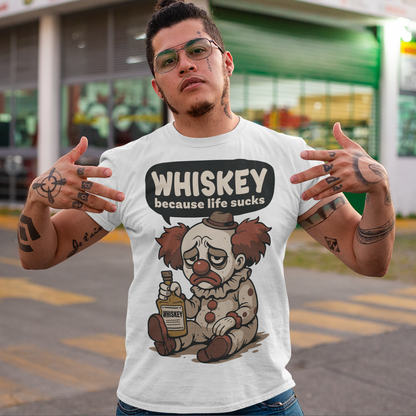 White t-shirt featuring a sad cartoon clown with messy red hair and a tired expression, sitting on the ground holding a bottle labeled whiskey. Above the character, bold text reads “Whiskey because life sucks.” The design combines dark humor with a playful cartoon style, creating a sarcastic and slightly edgy visual.