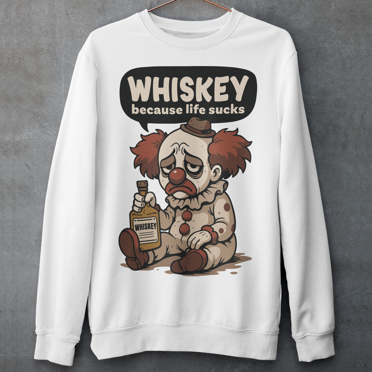 White sweatshirt featuring a sad cartoon clown with messy red hair and a tired expression, sitting on the ground holding a bottle labeled whiskey. Above the character, bold text reads “Whiskey because life sucks.” The design combines dark humor with a playful cartoon style, creating a sarcastic and slightly edgy visual.