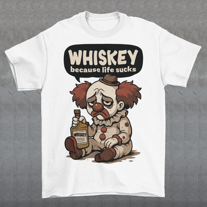 White t-shirt featuring a sad cartoon clown with messy red hair and a tired expression, sitting on the ground holding a bottle labeled whiskey. Above the character, bold text reads “Whiskey because life sucks.” The design combines dark humor with a playful cartoon style, creating a sarcastic and slightly edgy visual.