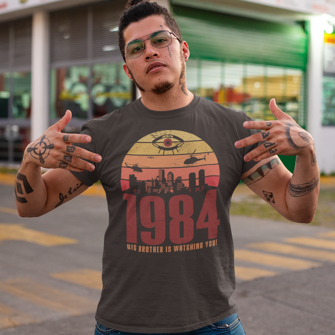 A brown t-shirt with a design of a sunset with dystopian silhouette with text underneath "1984 BIG BROTHER IS WATCHING".